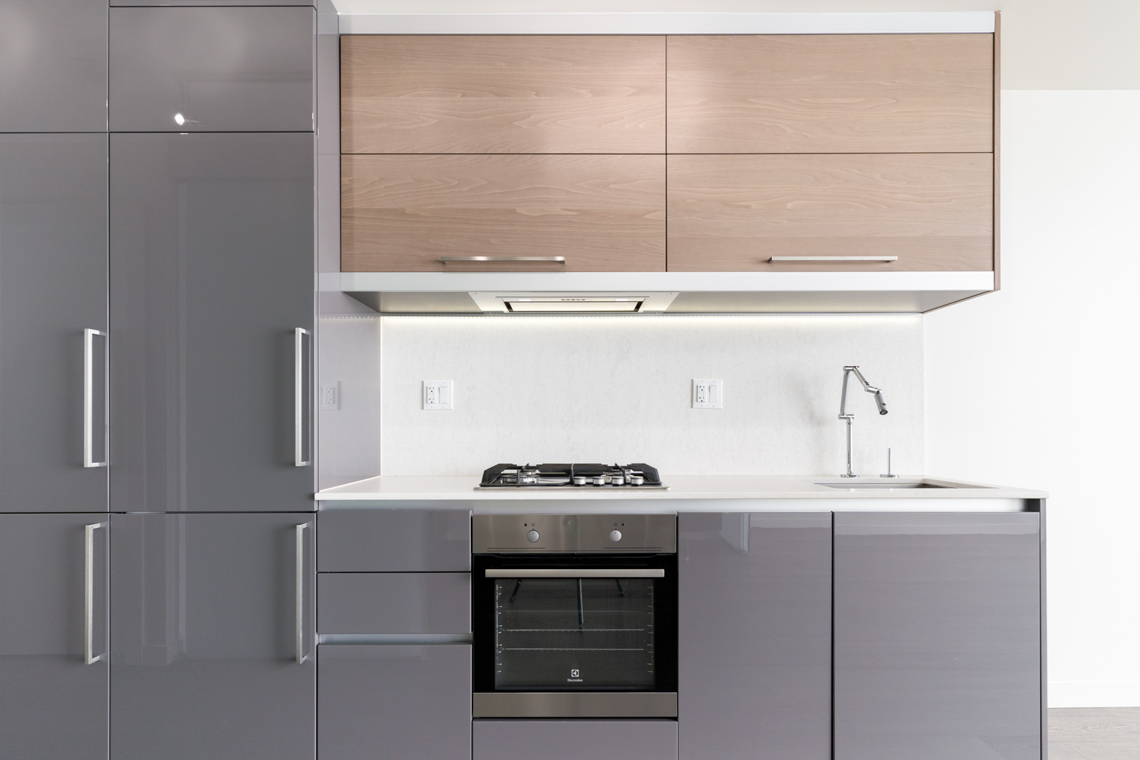 Modern kitchen with stainless steel appliances, gray cabinets, a gas stove, and a sink. Light wooden upper cabinets complement the sleek design.