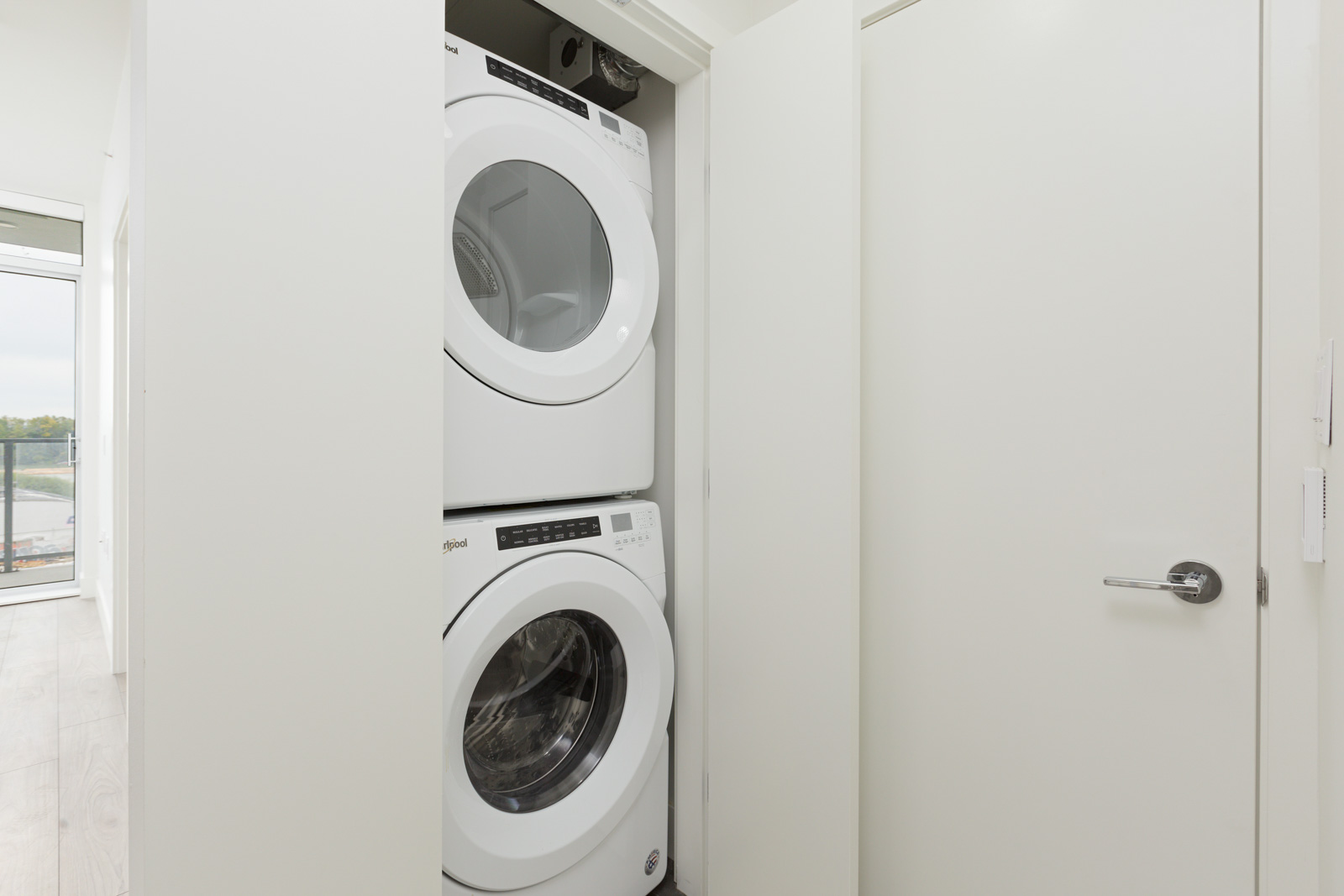 Stacked washer and dryer units in a closet with white doors open, revealing the appliances inside a brightly lit room.