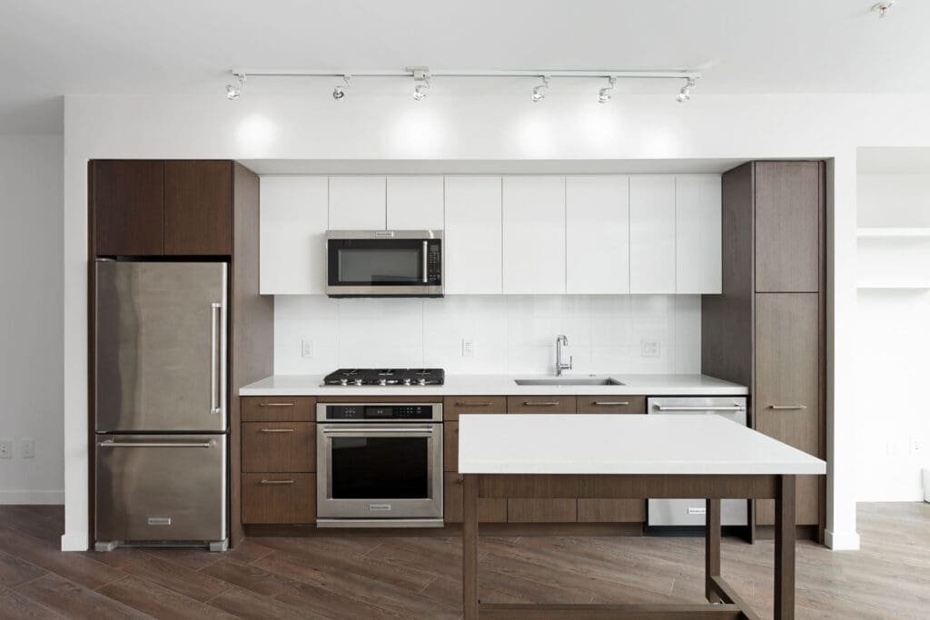 Modern kitchen with stainless steel appliances, white upper cabinets, brown lower cabinets, white countertop, and a central island.