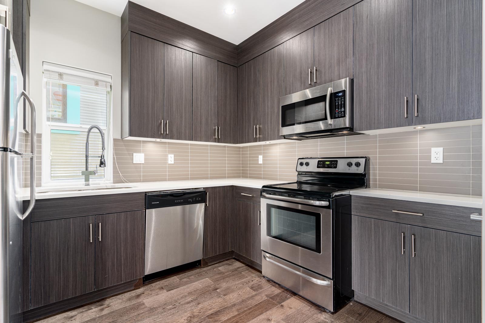 Modern kitchen with gray cabinetry, stainless steel appliances including a stove, microwave, and dishwasher, and beige tiled backsplash.
