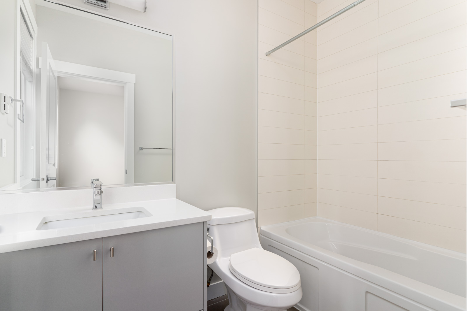 Modern bathroom with a white sink on a vanity, a toilet, and a bathtub with a shower rod. A large mirror is above the sink, and a towel rack is visible on the wall.