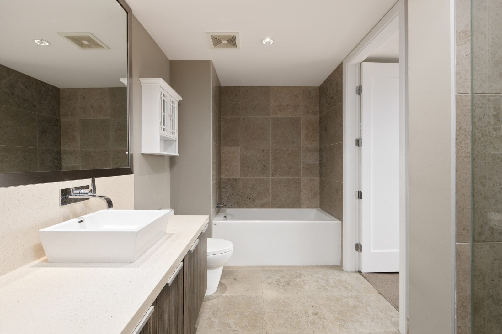 Modern bathroom with a white sink, countertop, and toilet, a bathtub with tiled walls, and a large mirror above the vanity.