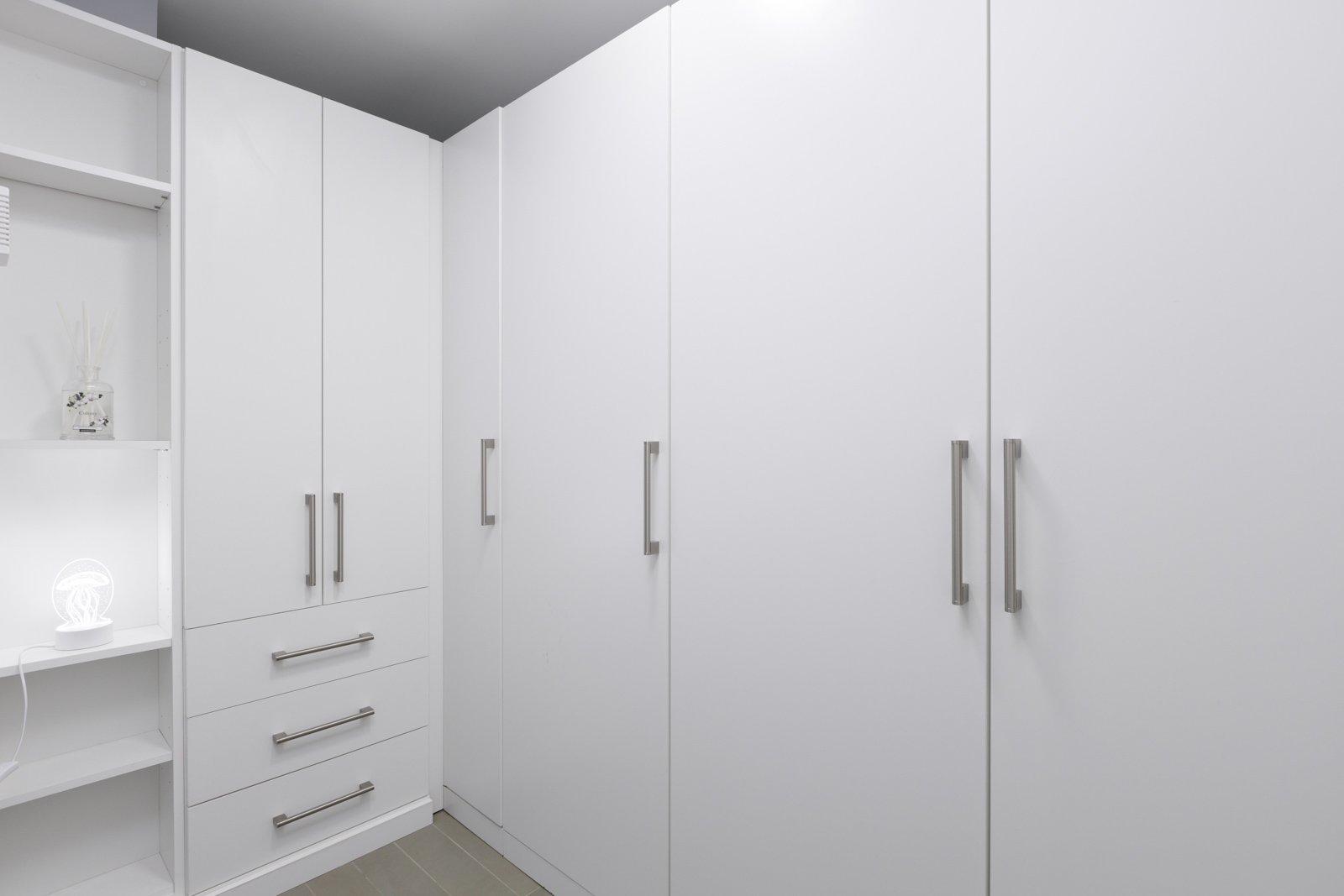 A white, modern wardrobe with closed cabinets, drawers, and a small open shelf with decorative items.