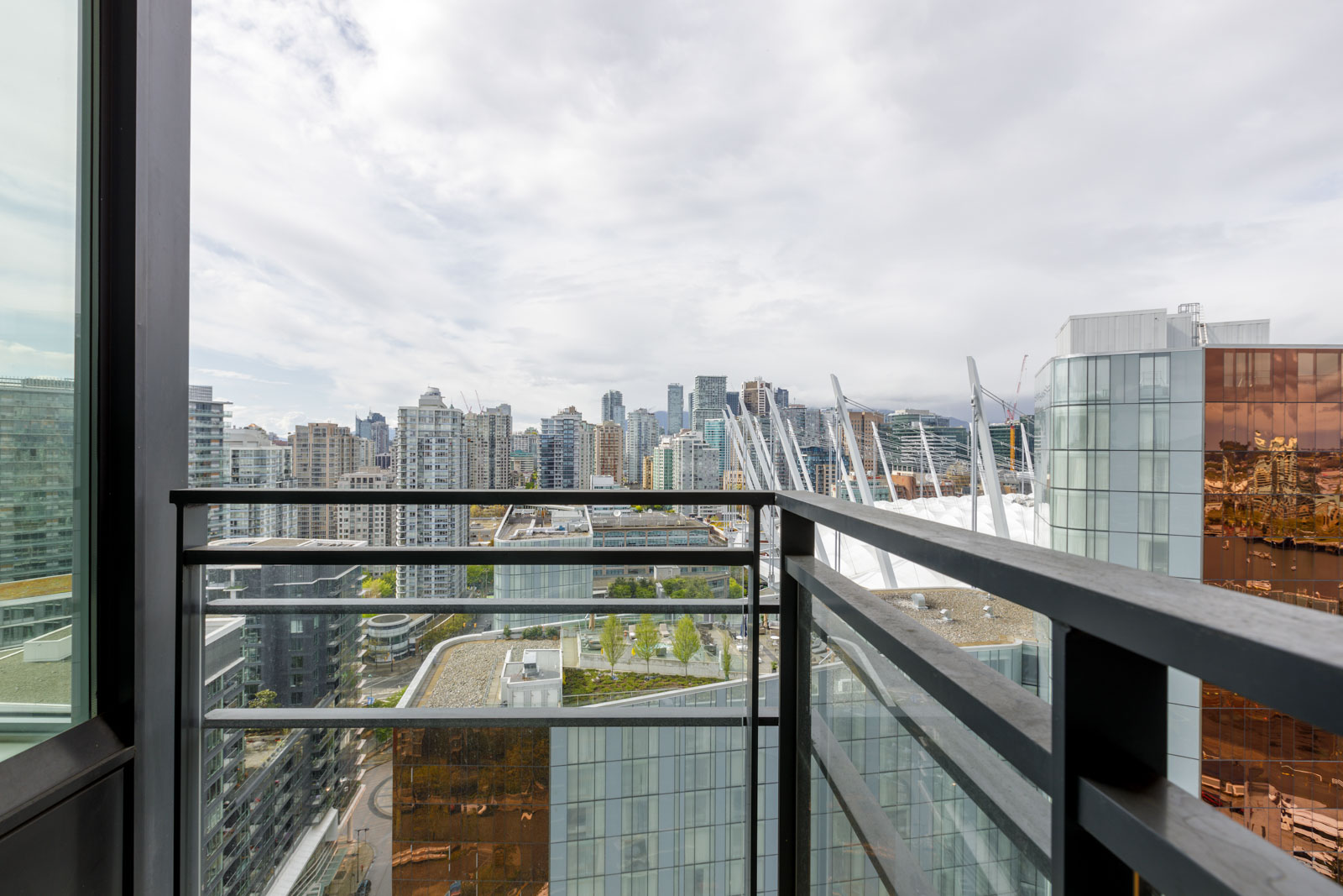 View from a high-rise balcony overlooking city skyscrapers and buildings under a cloudy sky.