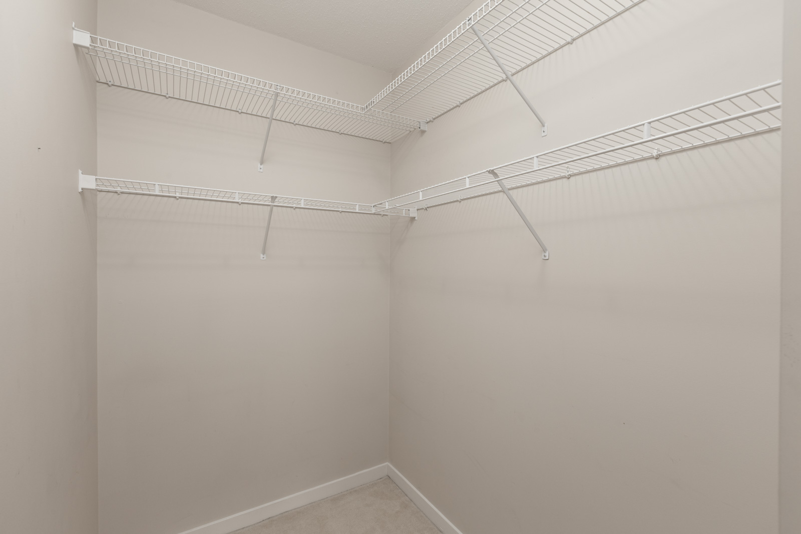 Empty walk-in closet with white wire shelving on beige walls.