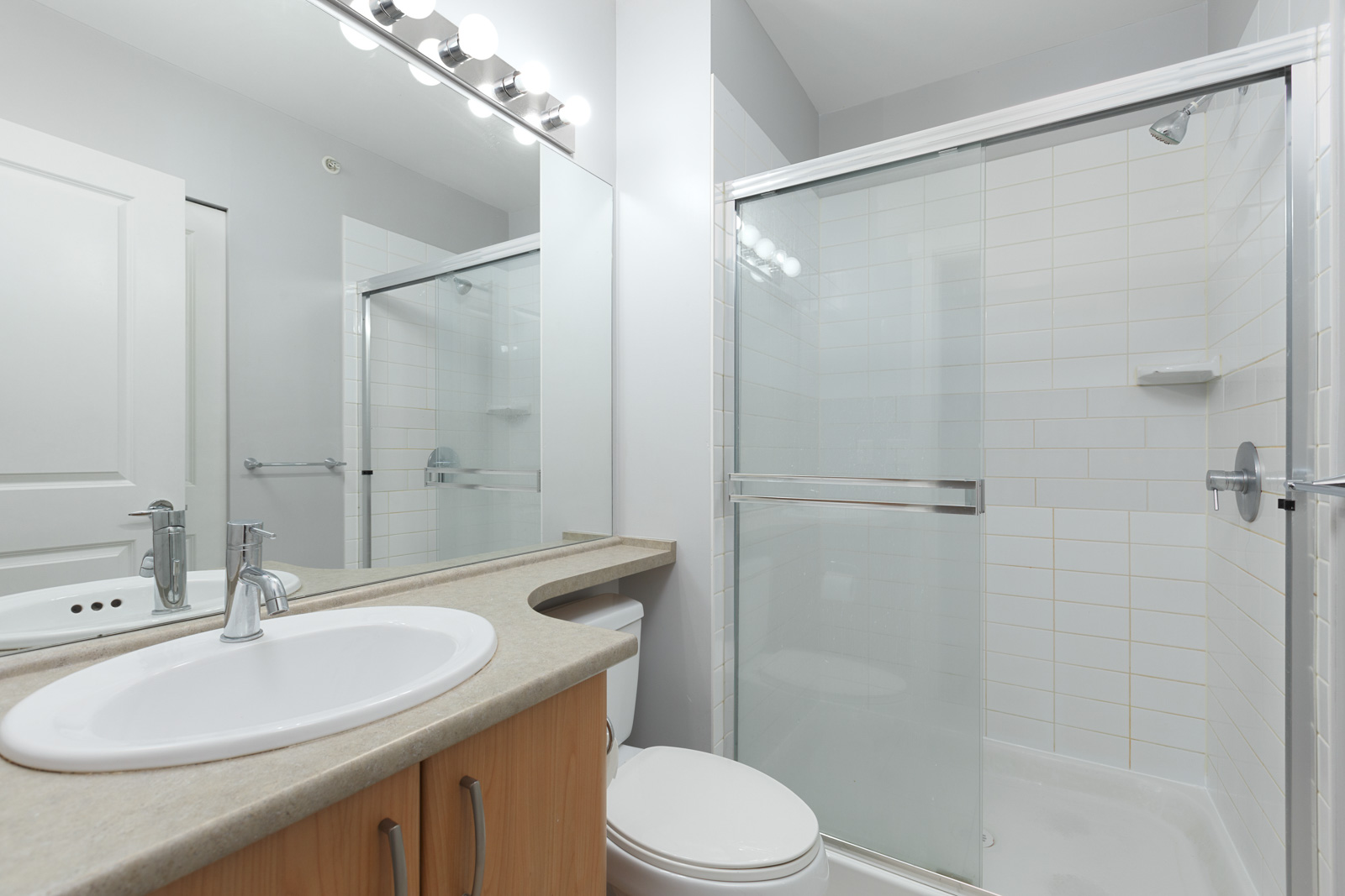 A modern bathroom with a sink, a countertop, a toilet, and a glass-enclosed shower with white tiles.