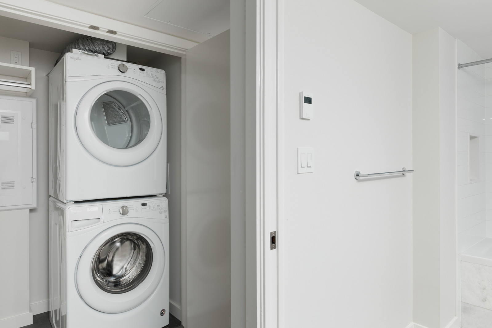 A stacked washer and dryer are installed in a closet next to a white wall and towel rack in a modern laundry area.