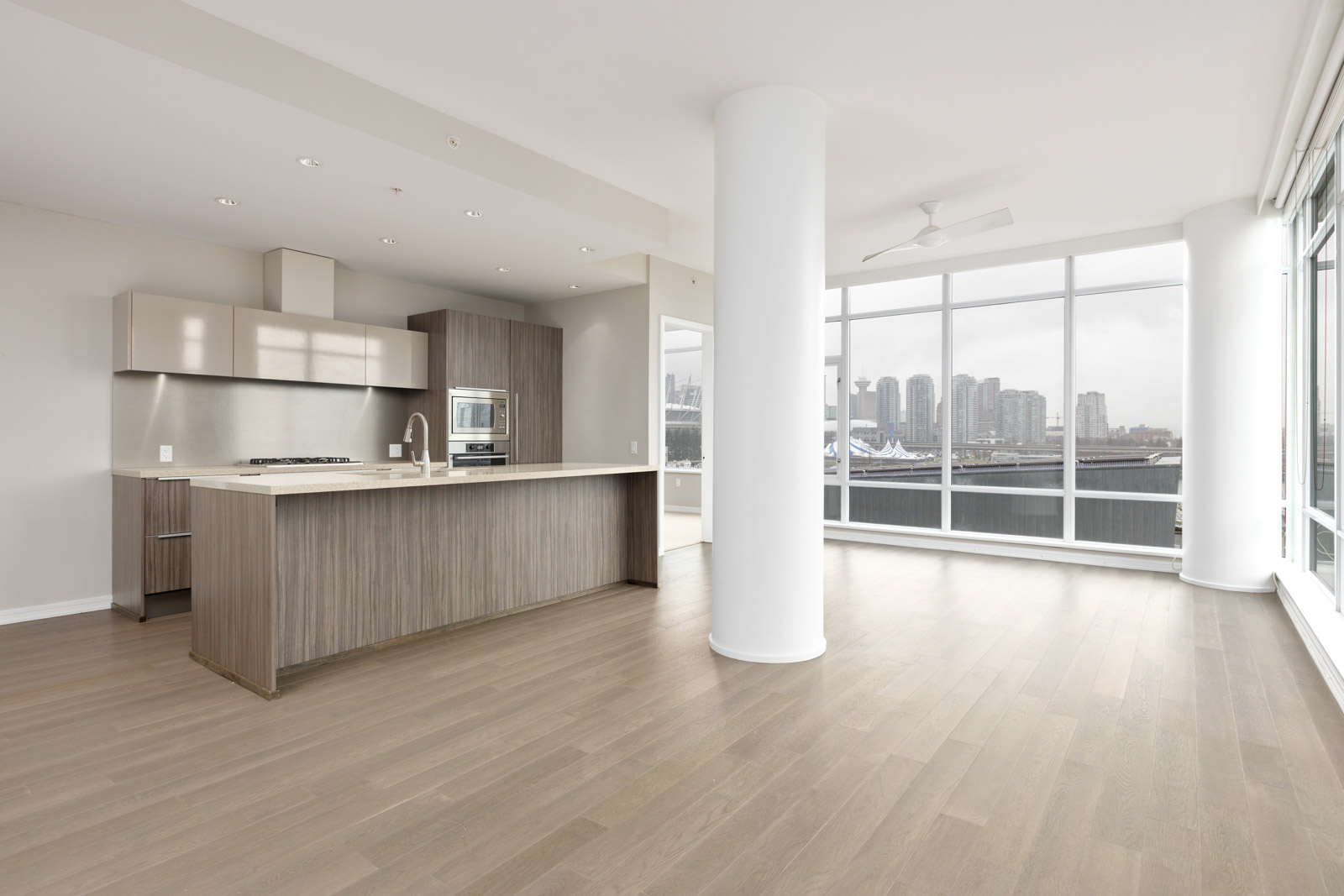 Modern open-concept kitchen and living area with floor-to-ceiling windows, light wood flooring, and a cityscape view.