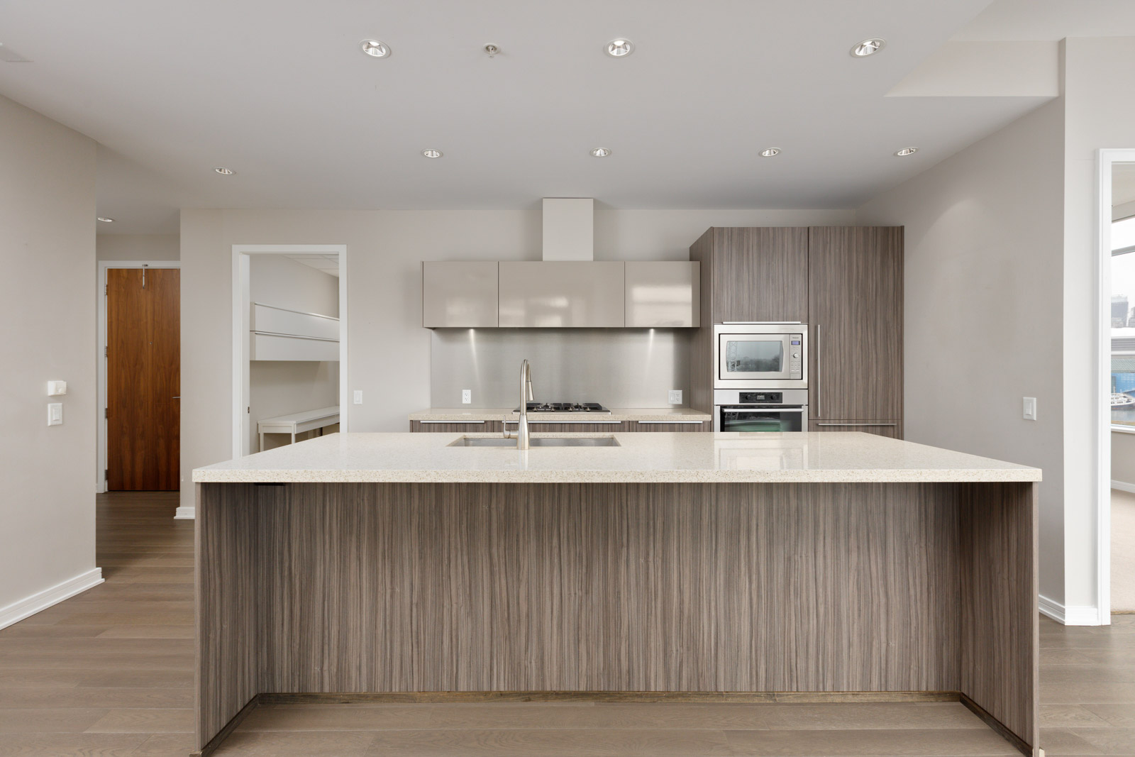 Modern kitchen with a large island, stainless steel appliances, and wood cabinetry. Neutral color scheme and overhead lighting.