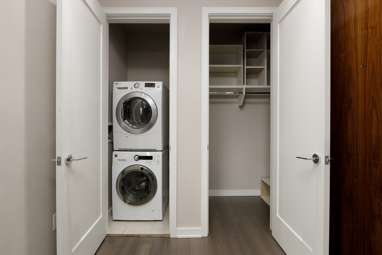 Laundry area with a stacked washer and dryer on the left, open closet with shelves and hanging space on the right, and wooden flooring.