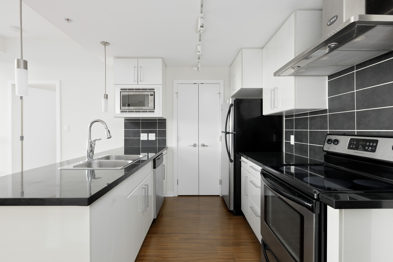 Modern kitchen with black countertops, white cabinets, stainless steel appliances, and wood flooring.