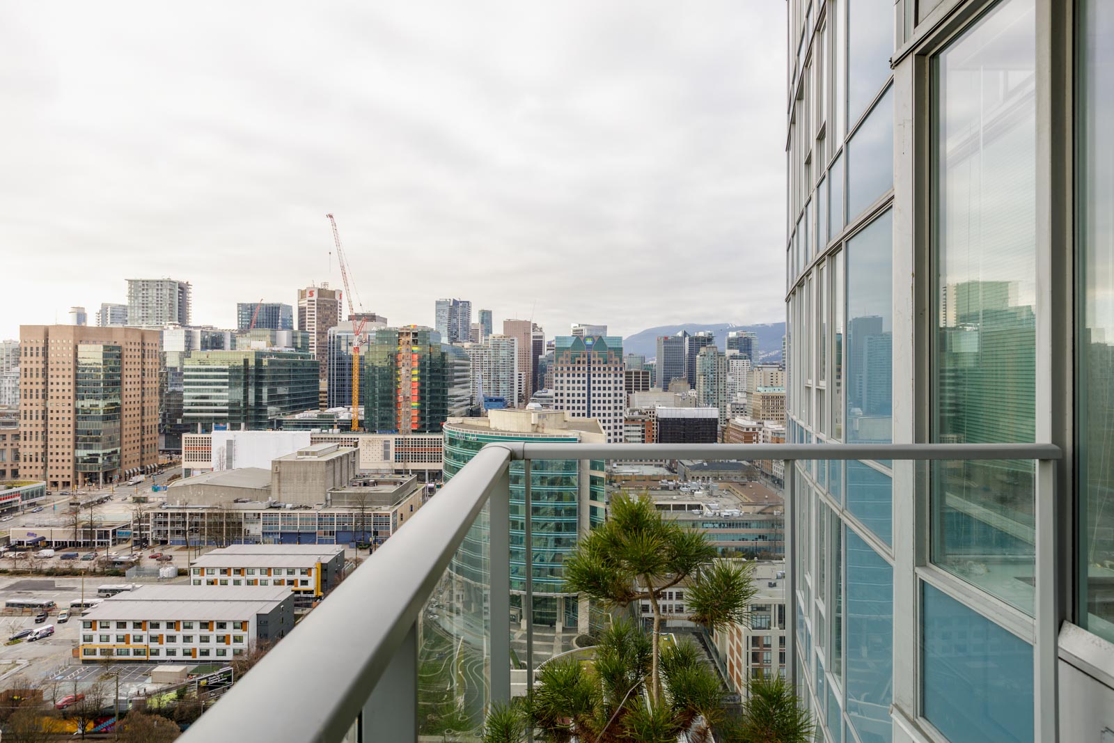 View from a balcony overlooking a cityscape featuring modern skyscrapers, construction cranes, and a partly cloudy sky.