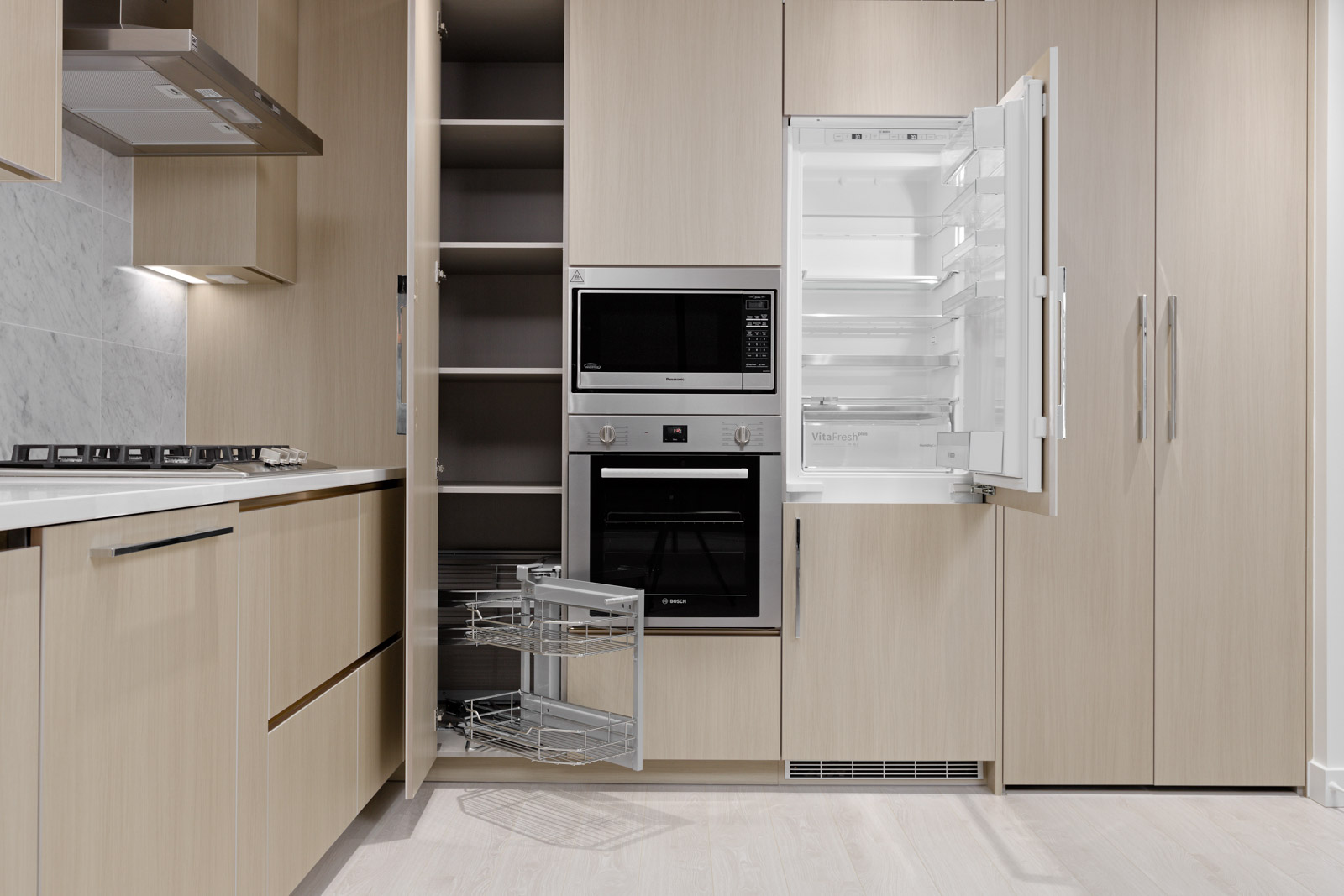 Modern kitchen with light wood cabinets, open fridge, built-in microwave, and oven. Pull-out drawer shown under stove.