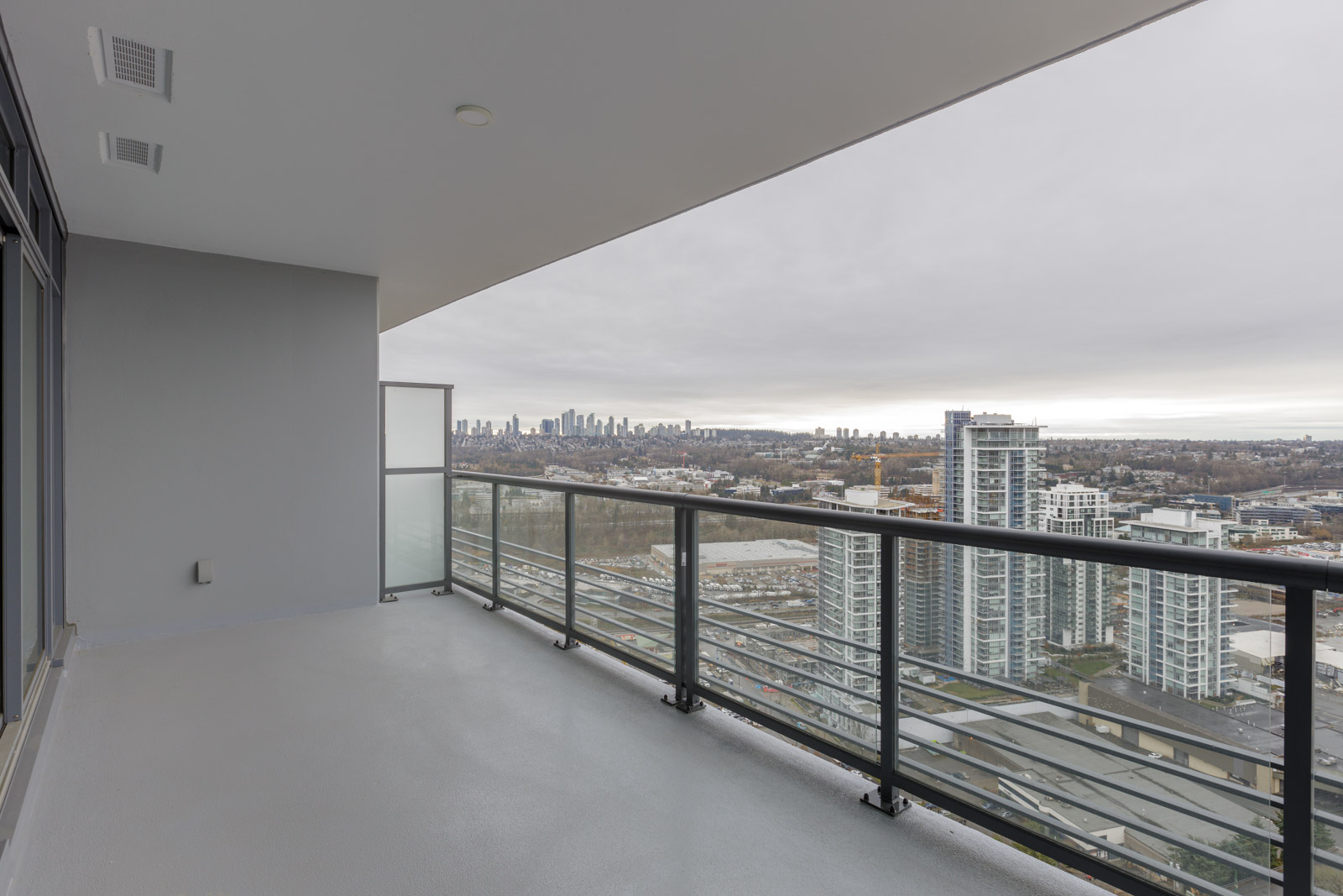 View from a high-rise balcony overlooking a cityscape with several tall buildings and a distant skyline under a cloudy sky.