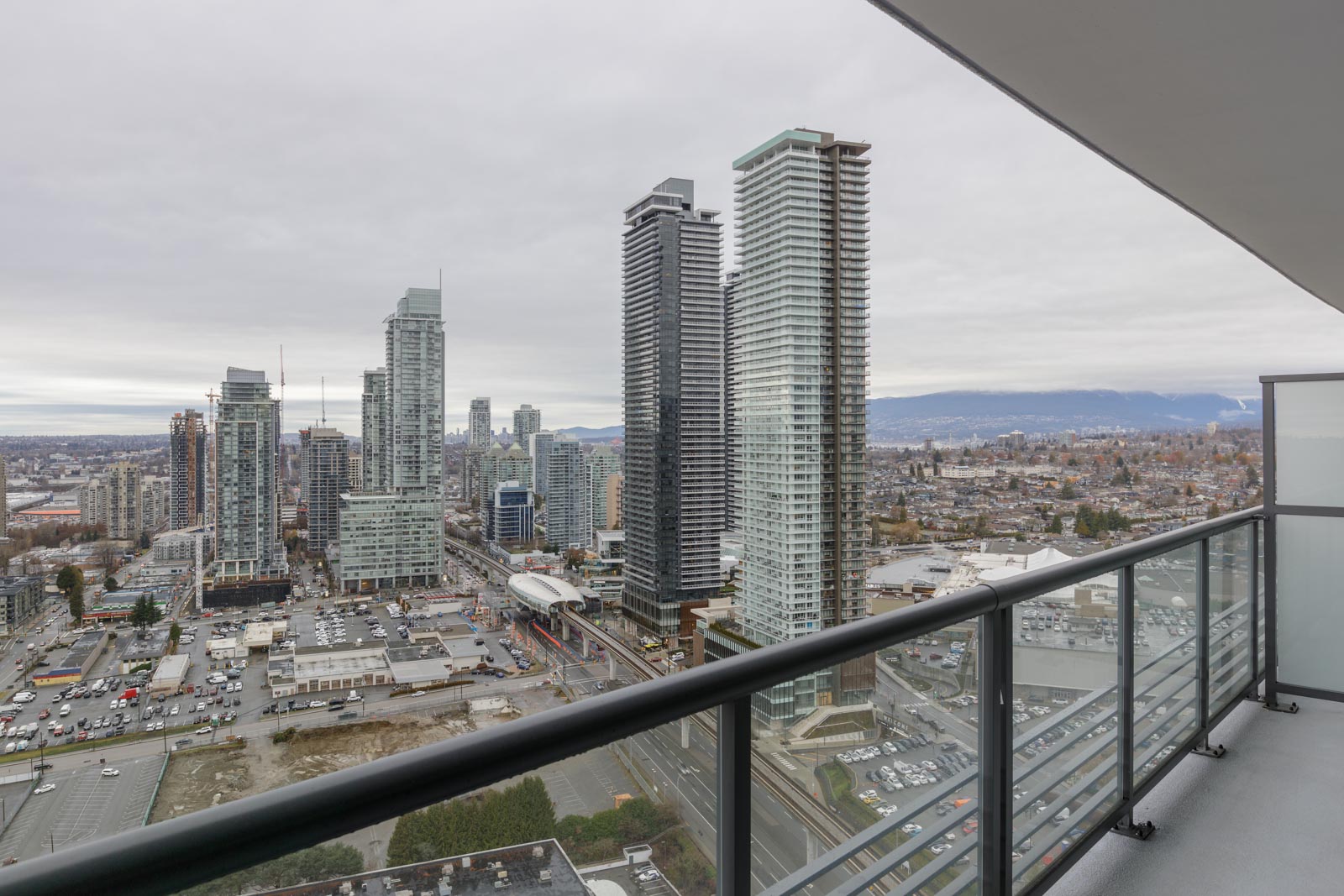 View from a high-rise balcony overlooking a cityscape with tall buildings, roads, and cloudy sky.