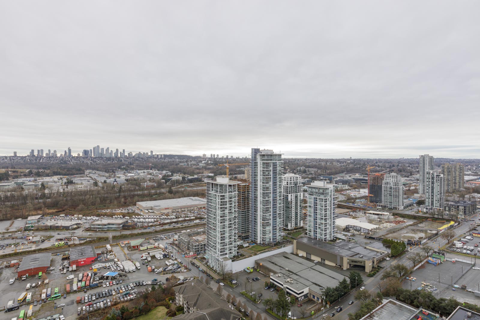 Aerial view of a cityscape with high-rise buildings, industrial areas, and distant skyline under a cloudy sky.