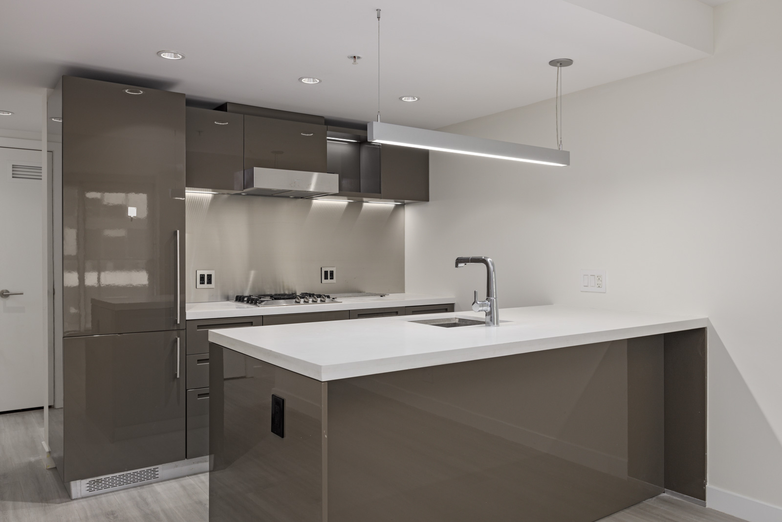 Modern kitchen with glossy grey cabinets, an island with a white countertop and built-in sink. The kitchen features stainless steel appliances, including a stove, oven, and built-in microwave.