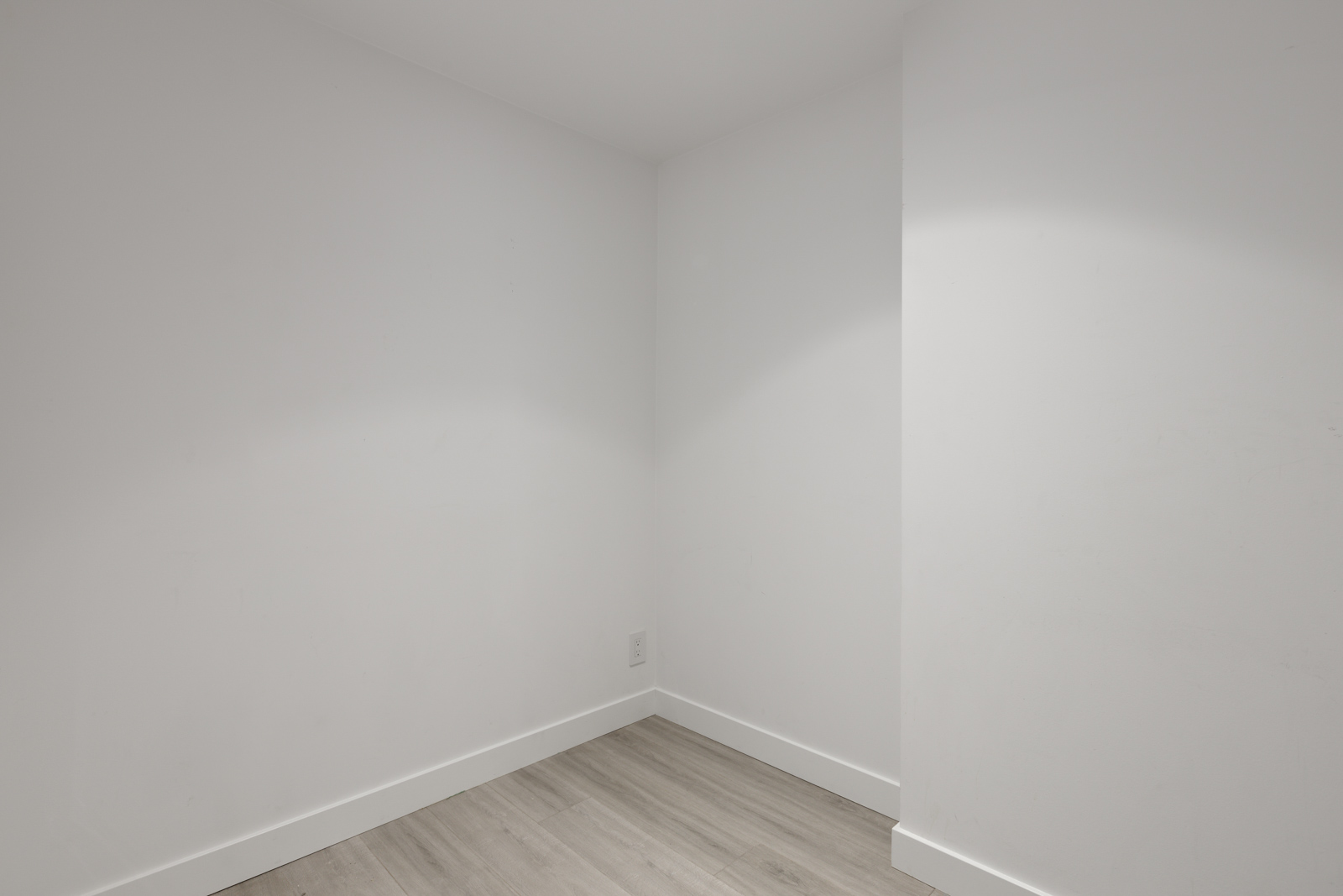 Empty corner of a white room with light gray flooring and a small section of divided wall.