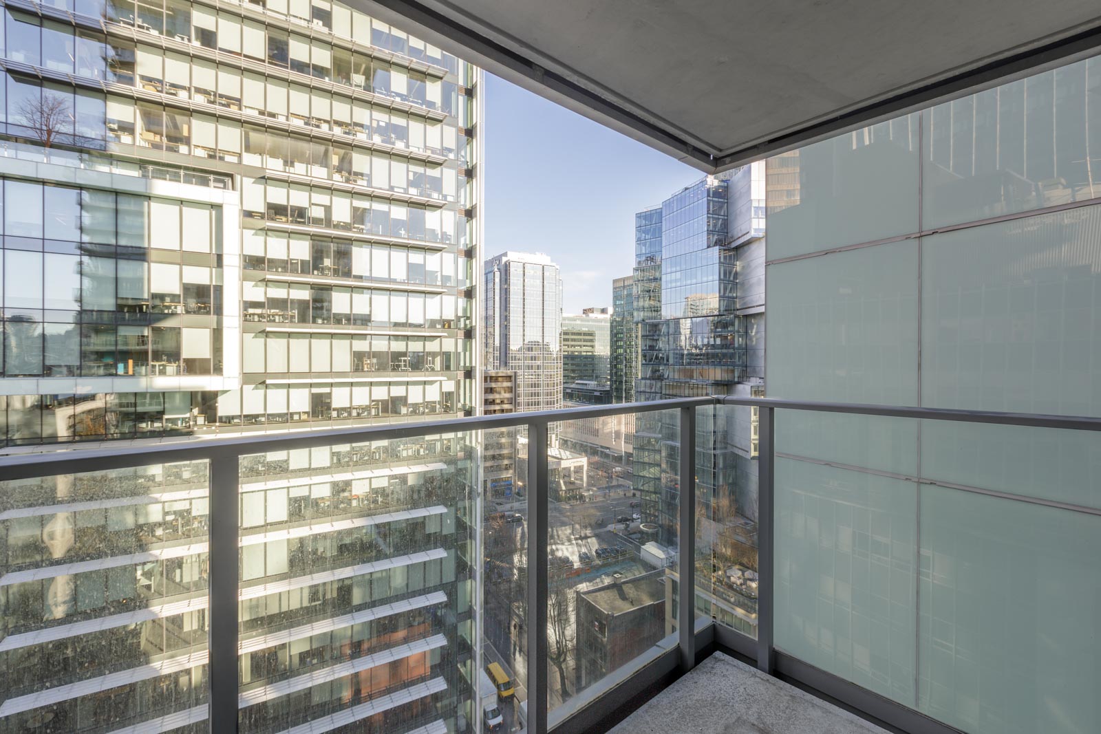 View of city buildings from a balcony with glass railings under partial shade.