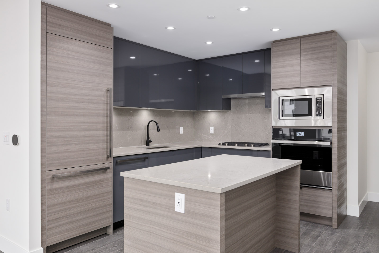 Modern kitchen with gray cabinets, sleek countertops, built-in appliances, and a central island. Ceiling lights illuminate the clean, minimalist design.