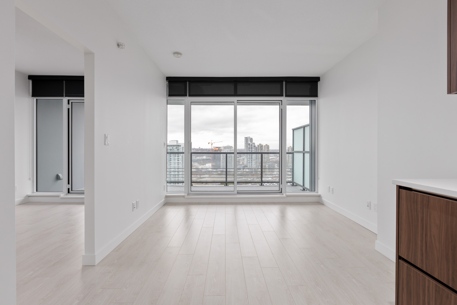 Unfurnished modern apartment with light wood floors, large floor-to-ceiling windows, and a cityscape view.