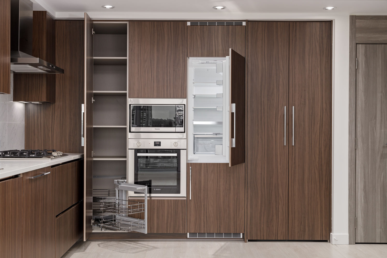 Modern kitchen with wood-paneled cabinets, open shelves, built-in oven, pull-out metal rack, and an open refrigerator integrated into the cabinetry.