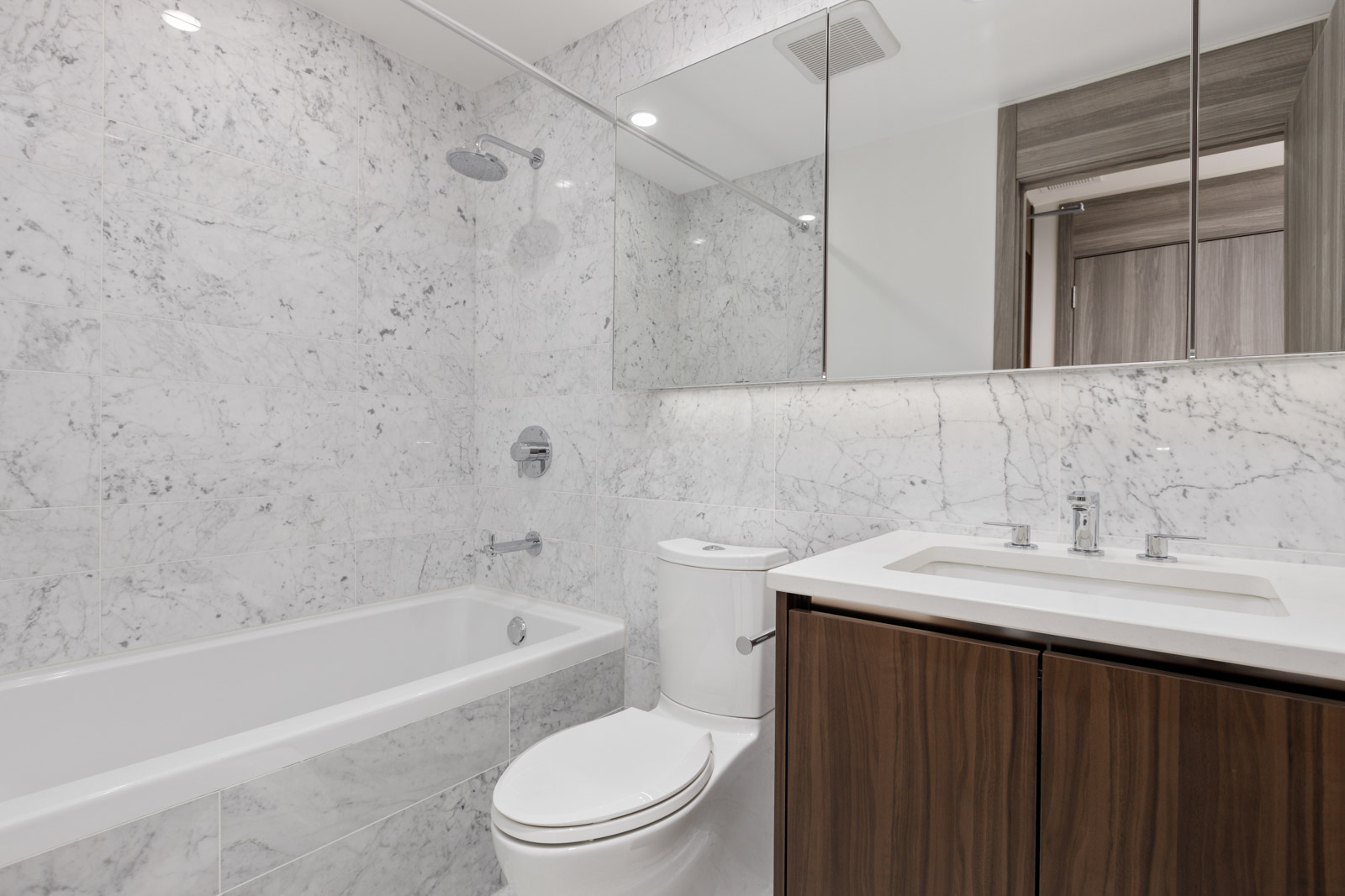 Modern bathroom with marble walls, a bathtub with shower, a toilet, and a vanity with a sink and large mirror above.