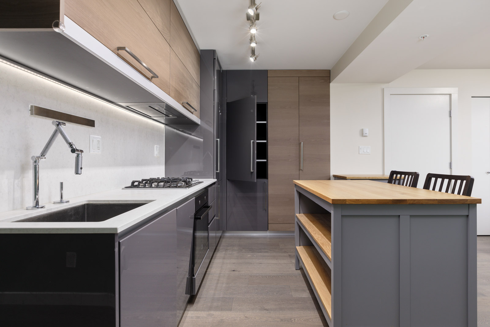Modern kitchen with wood and gray cabinetry, an island with a wooden countertop, gas stove, wall-mounted faucet, and track lighting.