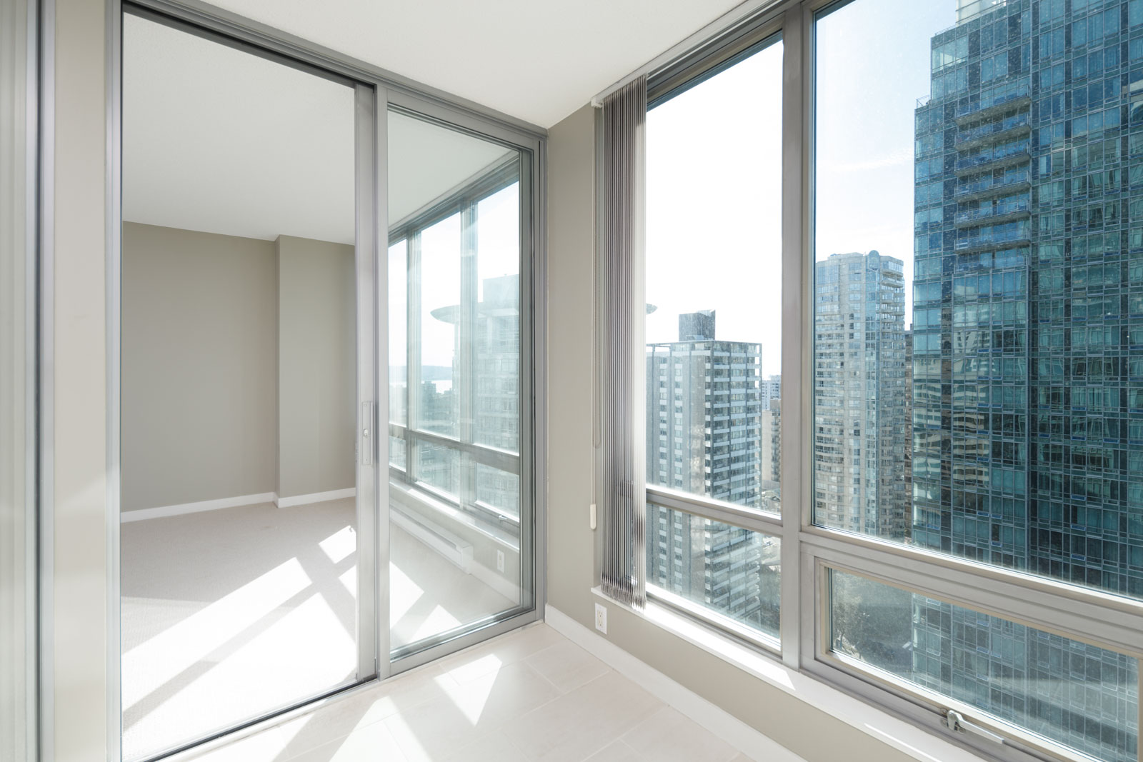 Modern high-rise apartment interior with floor-to-ceiling windows and sliding glass door, showing a view of city skyscrapers outside.
