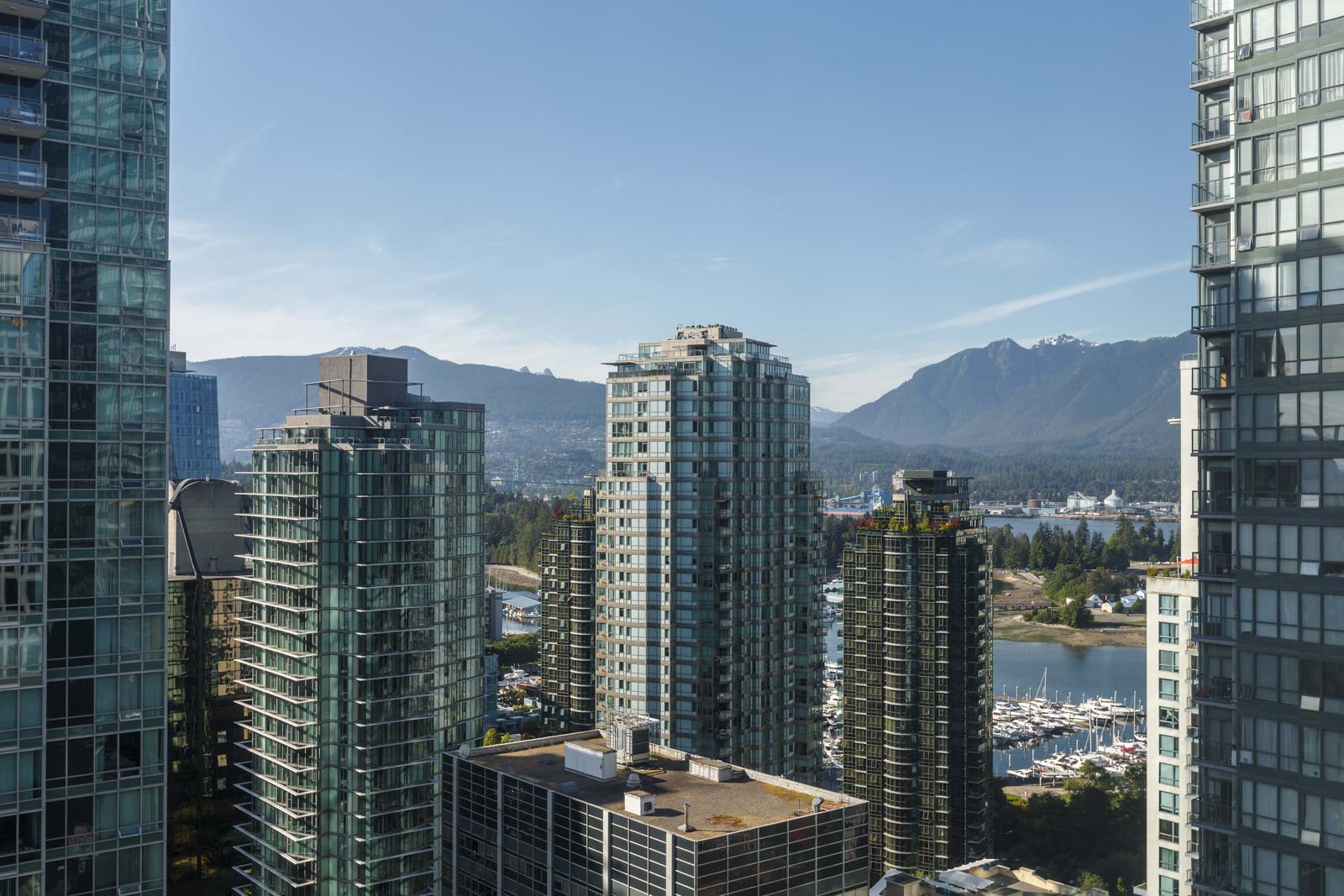 High-rise glass buildings with mountains and a marina visible in the background under a clear blue sky.