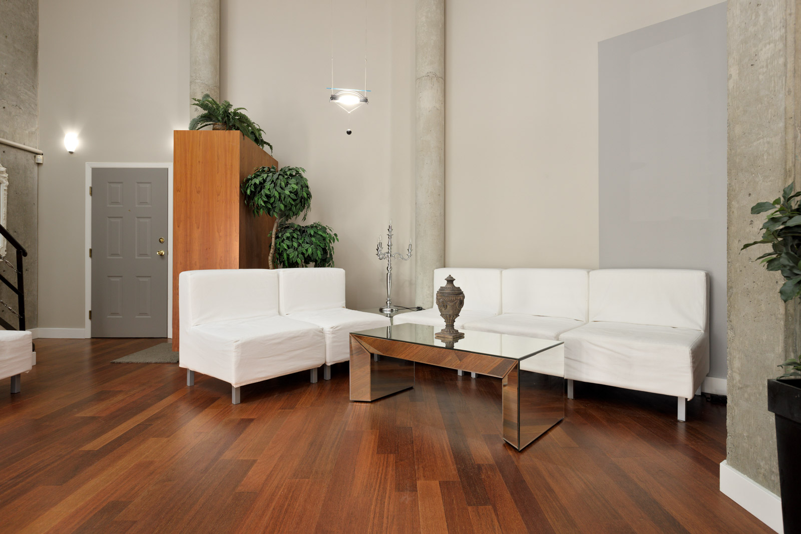 A modern living room with white sofas, glass coffee table, decorative plants, and a vase on the table, featuring wooden flooring and neutral wall tones.