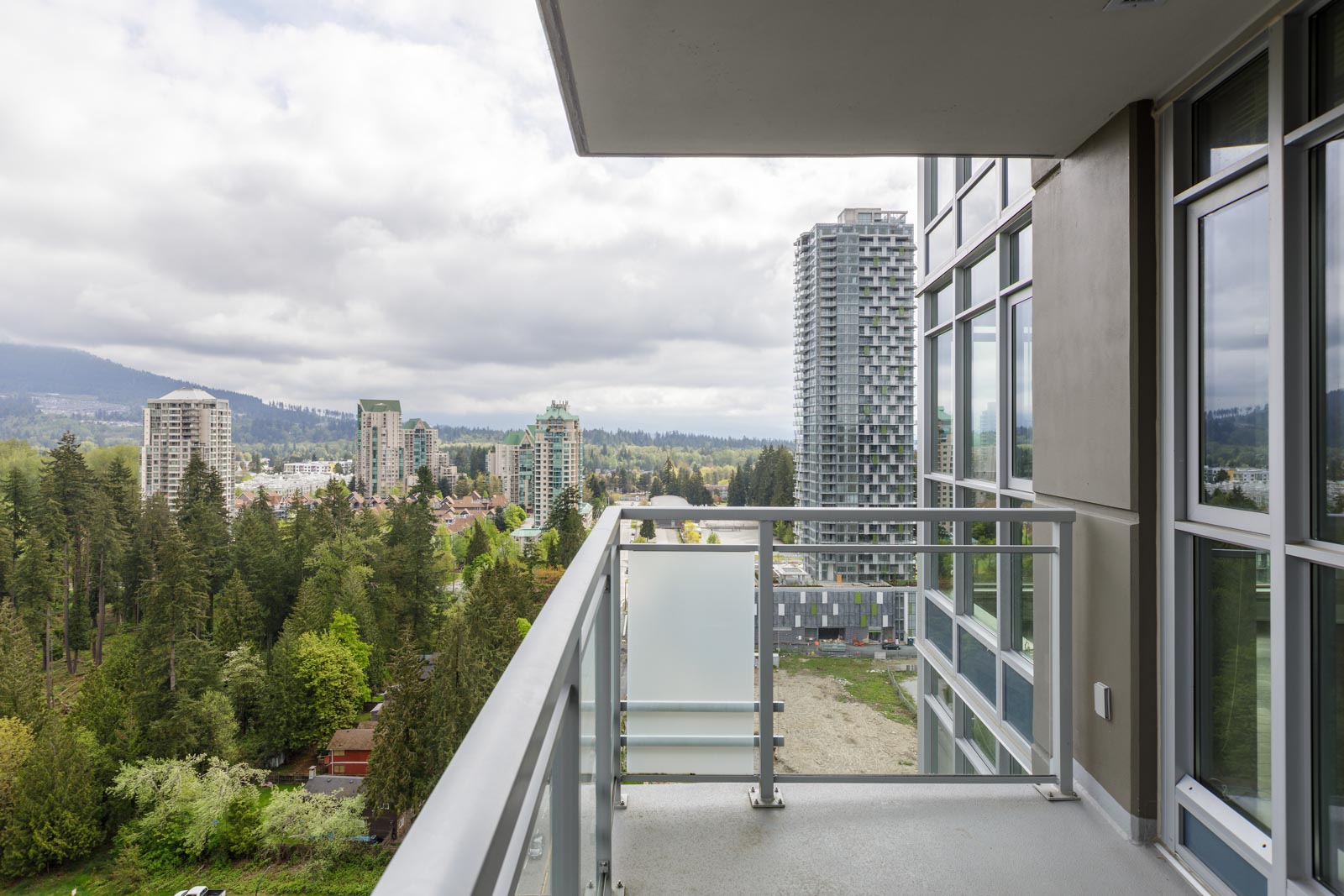 View from a balcony showing a cityscape with multiple high-rise buildings, trees, and a cloudy sky.