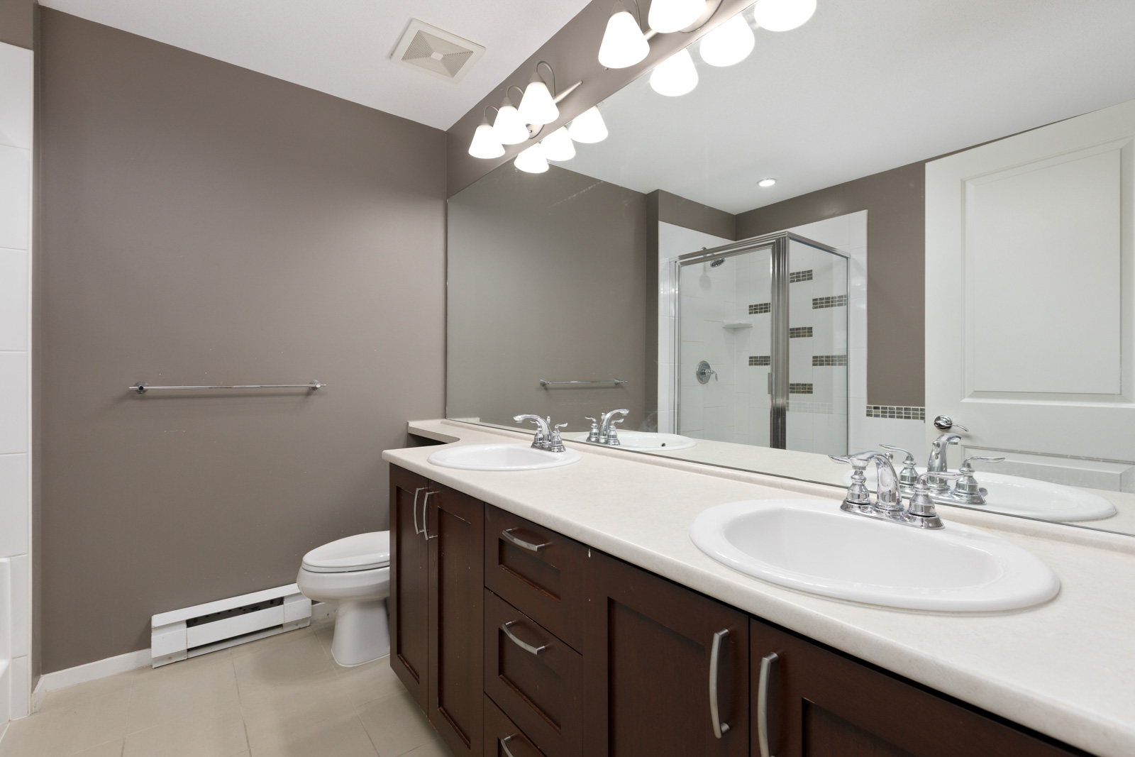 A modern bathroom features a double vanity with sinks, a large mirror, a glass-enclosed shower, and neutral-toned walls and tiles.