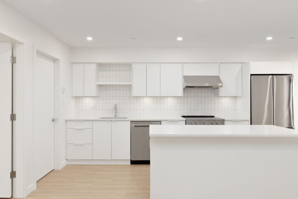 Modern kitchen with white cabinets, stainless steel appliances, tile backsplash, and a central island on light wood flooring under recessed lighting.