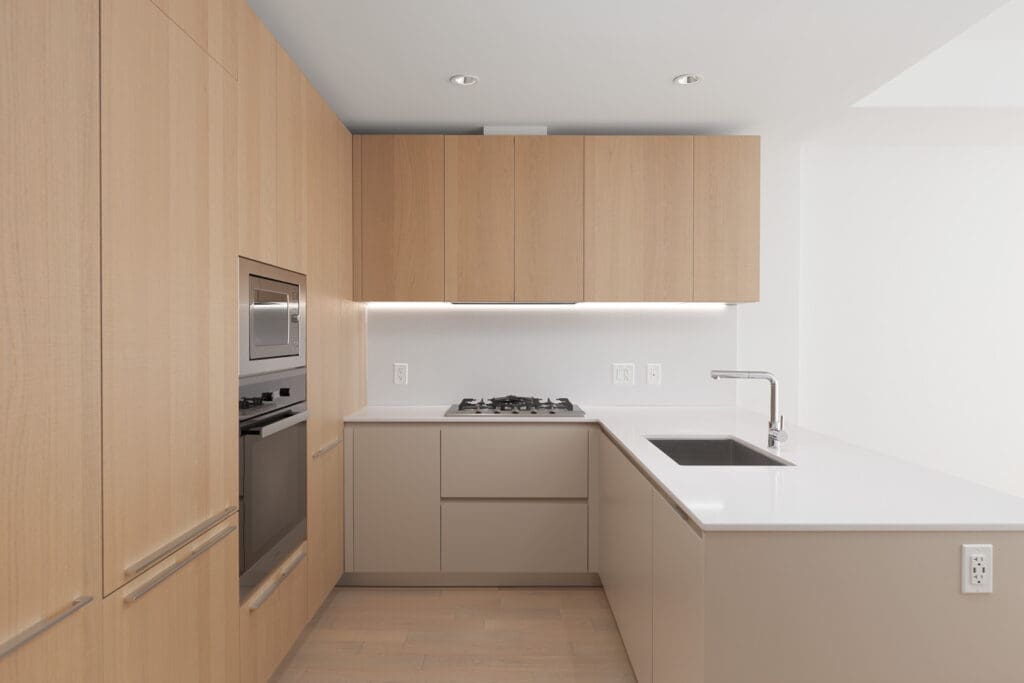 Modern kitchen with light wood cabinets, built-in oven, gas cooktop, stainless steel microwave, white countertops, and an under-mount sink. The space is clean and minimalistic.