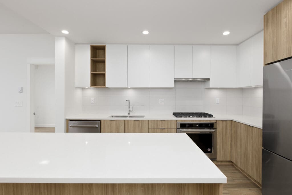 Modern kitchen with white cabinets, wooden accents, stainless steel appliances, and a large central island.