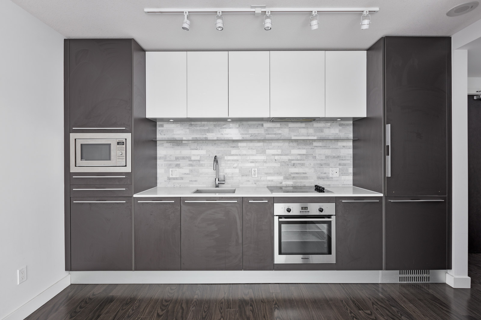 Modern kitchen with dark cabinets, white upper cupboards, stainless steel appliances, and a gray backsplash. Built-in oven and microwave are visible.