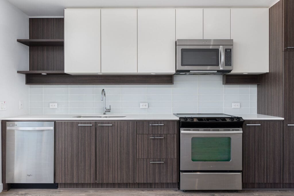 Modern kitchen with white and dark wood cabinets, stainless steel appliances, including a microwave, dishwasher, stove, and an undermount sink with a tiled backsplash.