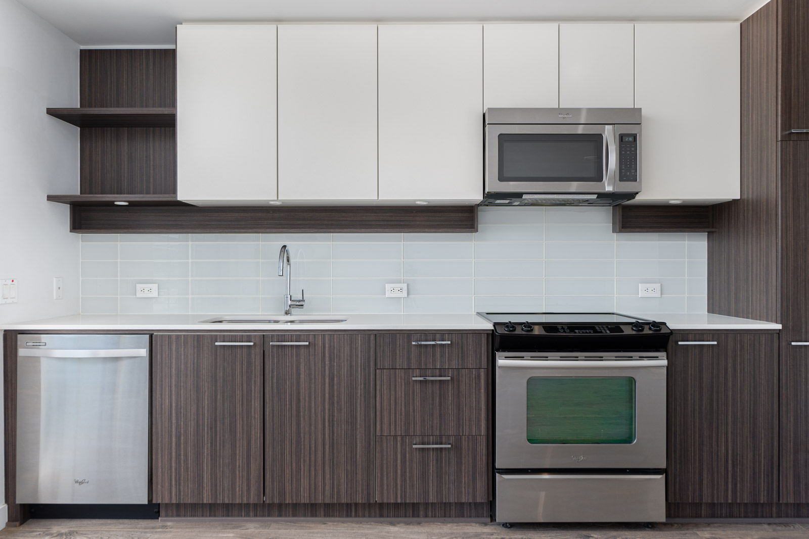 Modern kitchen with white and dark wood cabinets, stainless steel appliances, including a microwave, dishwasher, stove, and an undermount sink with a tiled backsplash.