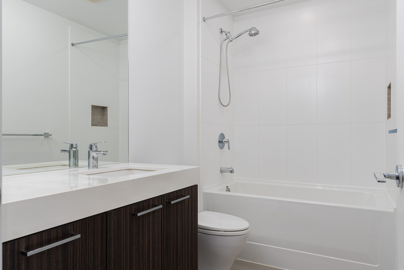 Modern bathroom with white walls, a bathtub-shower combo, a toilet, and a sink with a dark wood cabinet.