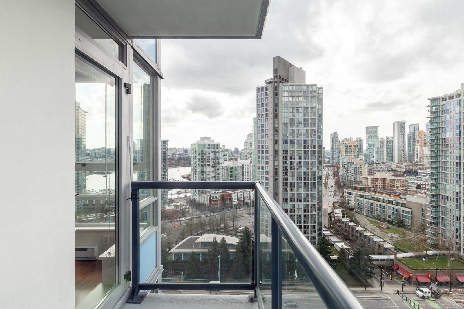 View from a high-rise balcony overlooking a cityscape with numerous modern buildings, a river in the distance, and a cloudy sky.