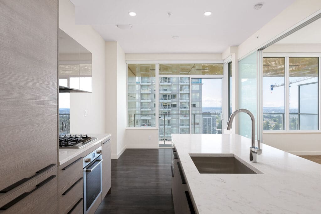 Modern kitchen with a marble island, stainless steel appliances, and large windows offering a city view.