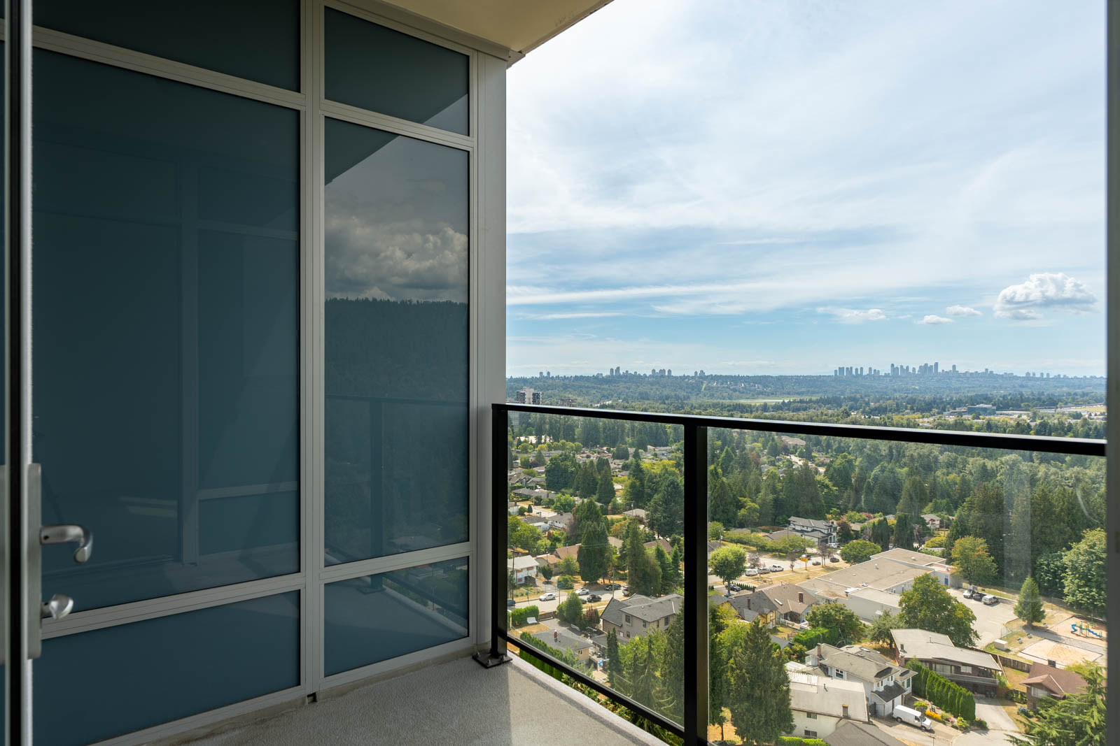 Balcony view overlooking a suburban landscape with trees and houses, distant city skyline under a partly cloudy sky.