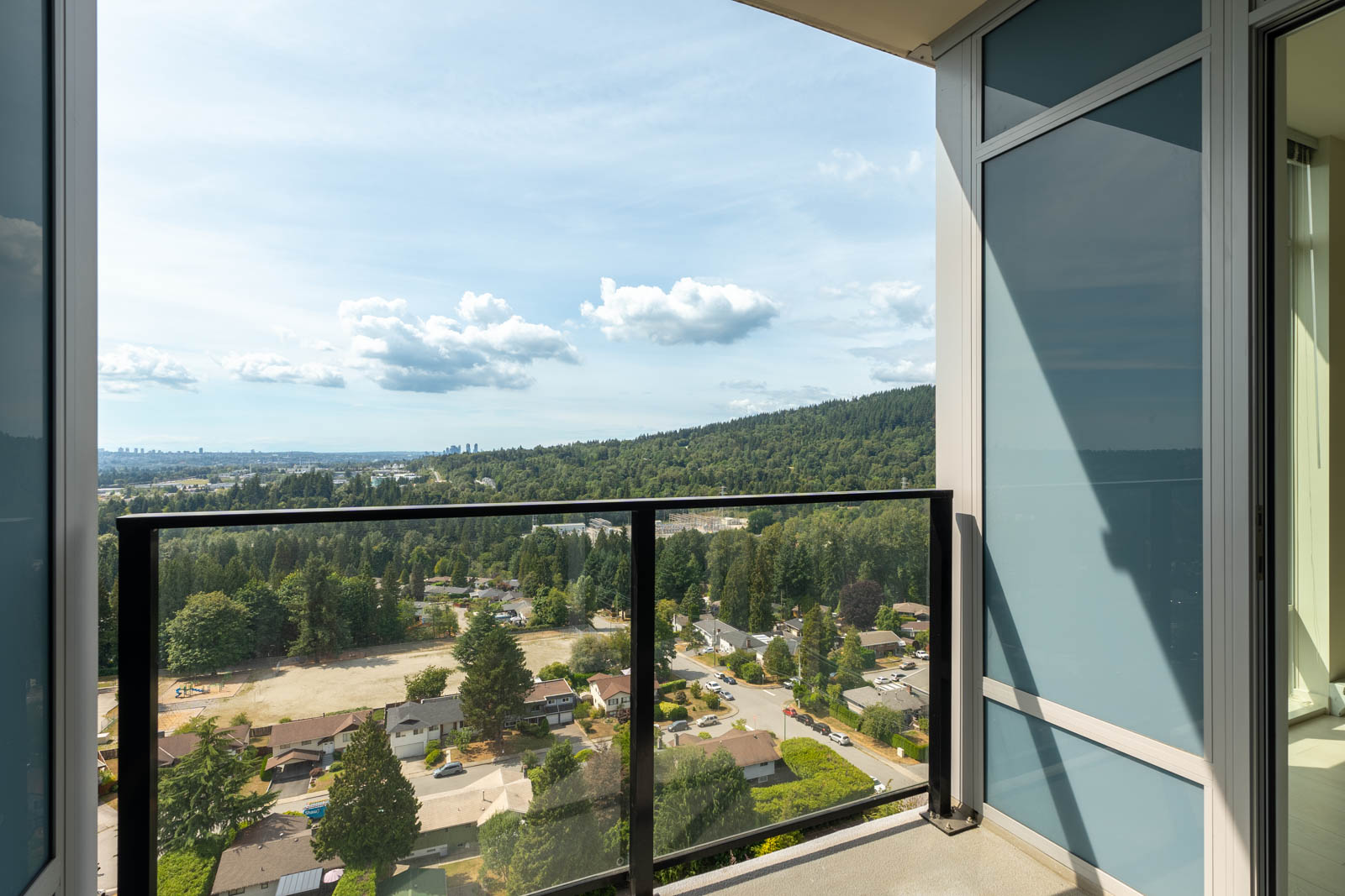 View from a balcony showing a suburban area with houses, trees, and rolling hills under a partly cloudy sky.