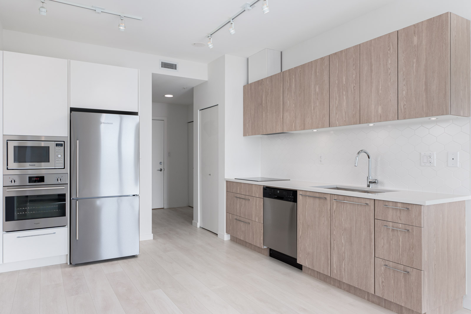 Modern kitchen with light wood cabinets, stainless steel appliances, white countertops, and a geometric tile backsplash.