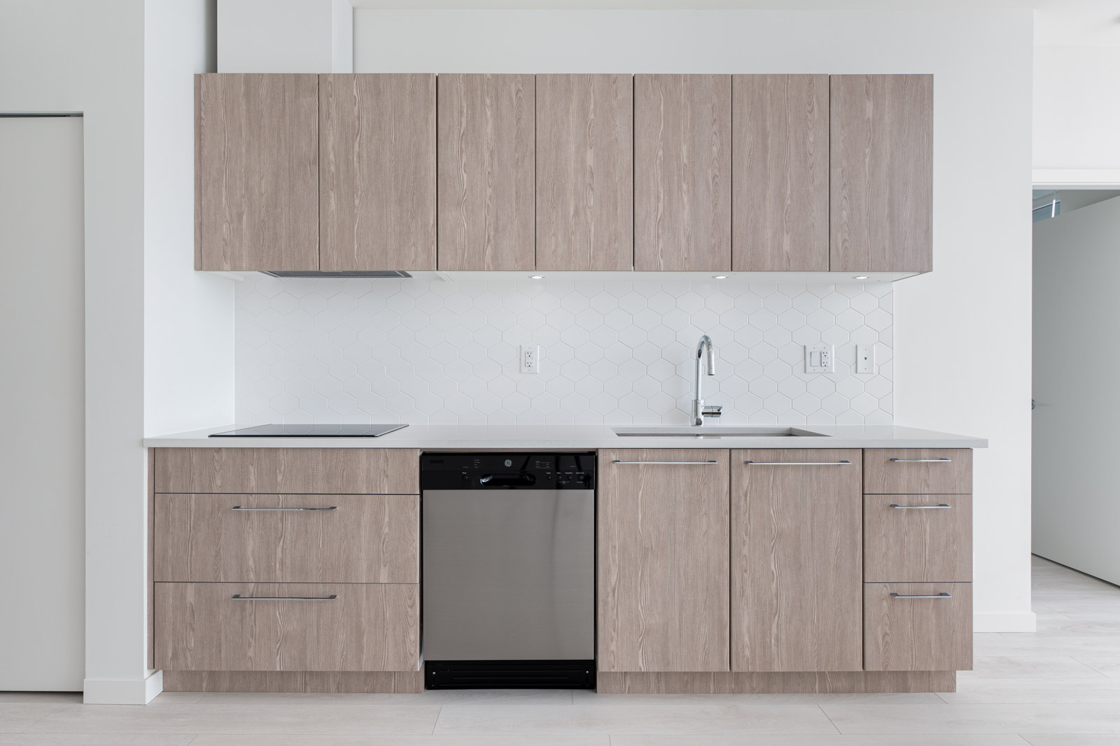 Modern kitchen with light wood cabinets, a white hexagonal tile backsplash, a sink with a chrome faucet, and a stainless steel dishwasher.