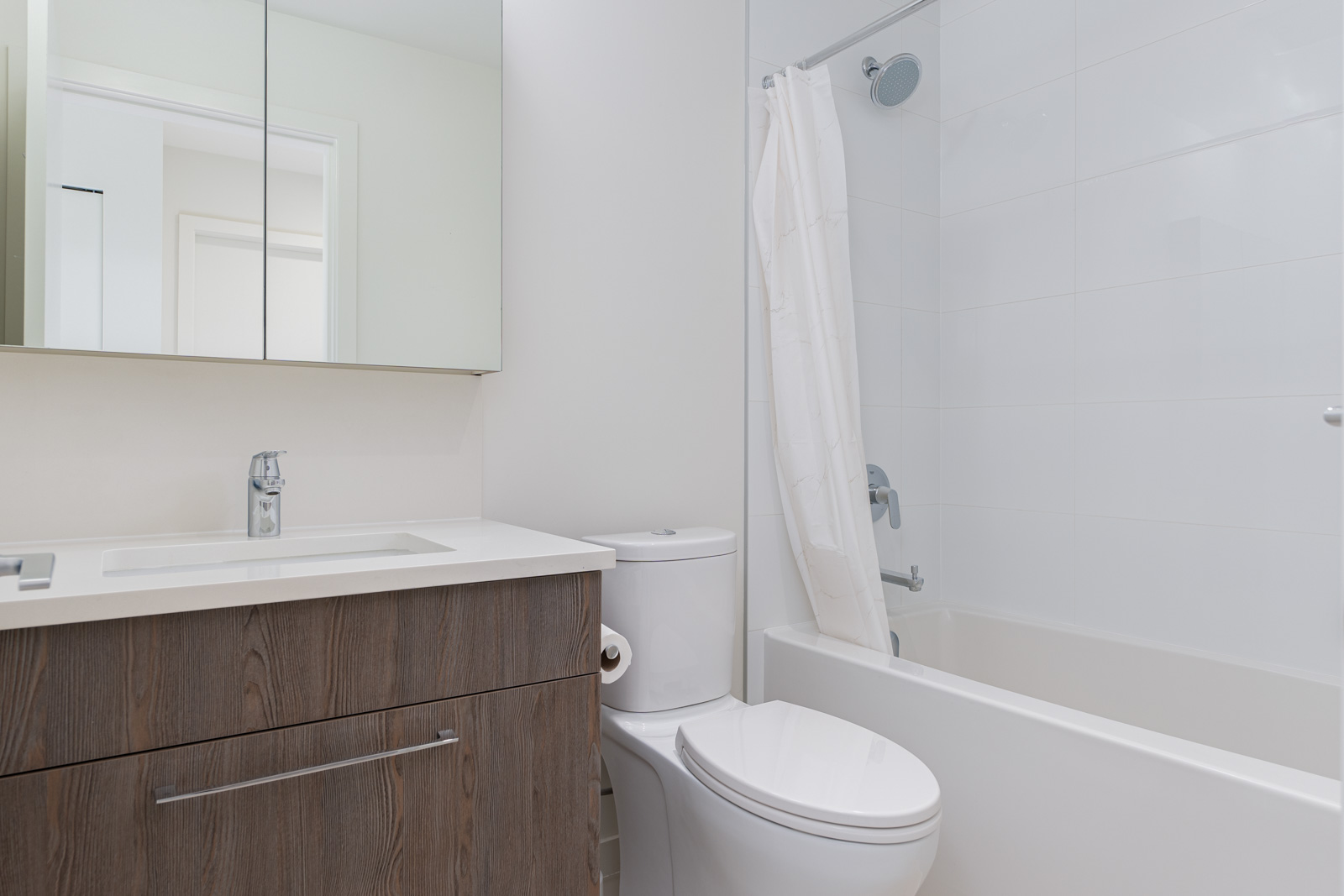A modern bathroom with a wooden vanity, mirror, toilet, and a bathtub with a white shower curtain.