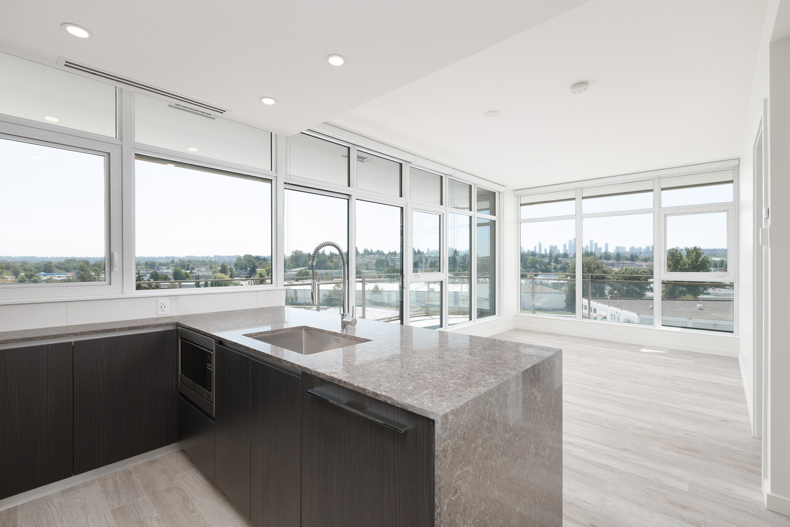 A modern kitchen with a large island and sink, surrounded by floor-to-ceiling windows offering a view of the city skyline and surrounding landscape.