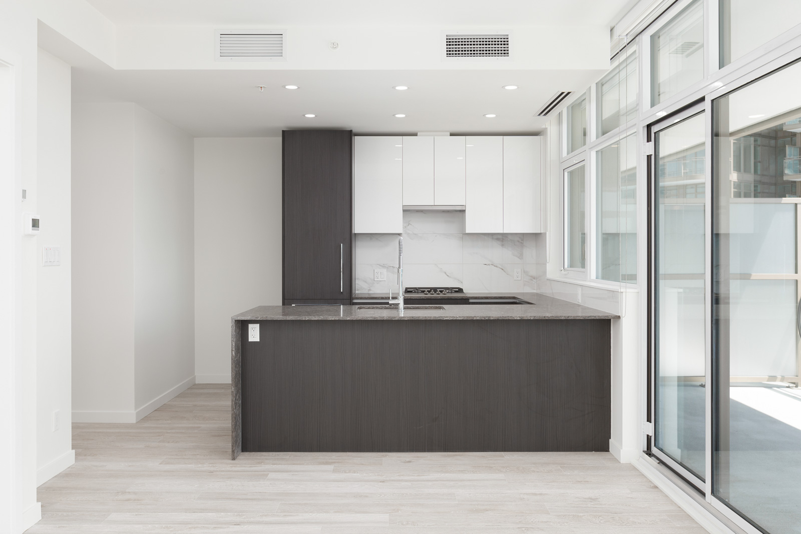 Modern kitchen with a dark island, white countertops and cabinets, stainless steel appliances, and large windows.