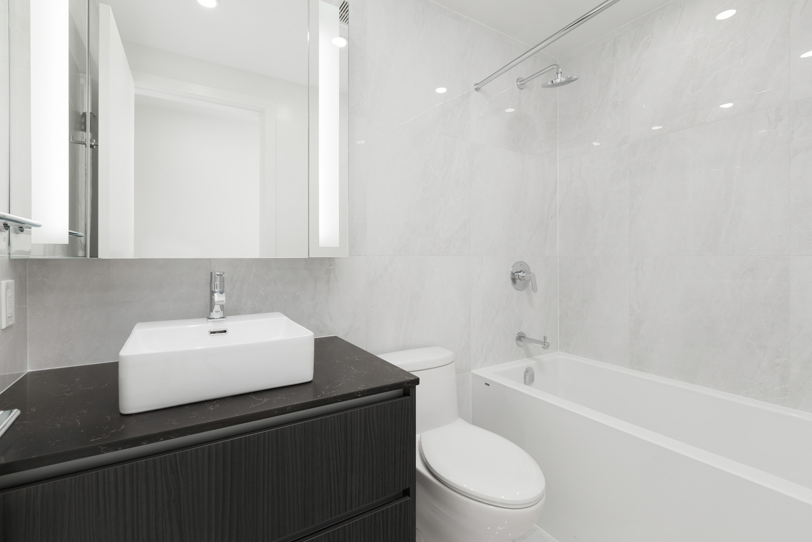 Modern bathroom with white walls, a black vanity with a rectangular sink, a toilet, and a bathtub with a showerhead.